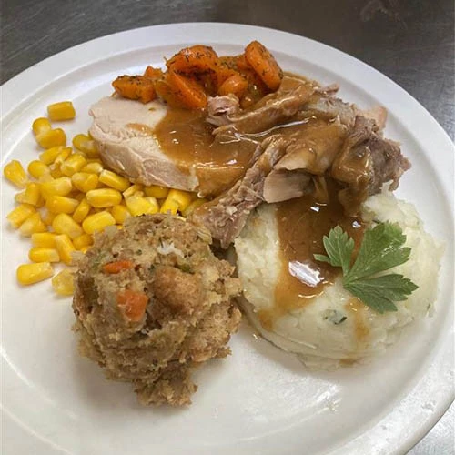 Thanksgiving plate featuring mashed potatoes, stuffing, corn, carrots, turkey, and gravy.