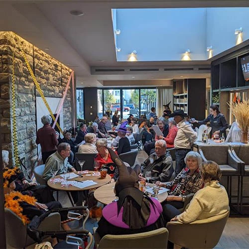 Lots of residents in a room together for Halloween. Most of the residents are wearing costumes and having fun together.