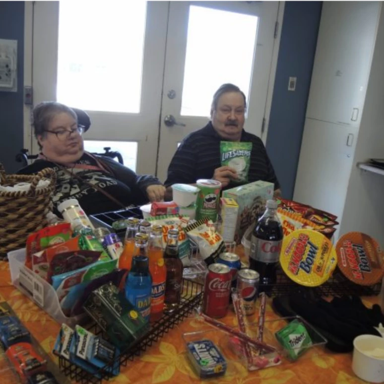 Two seniors seated at a table with a bunch of tasty snacks.