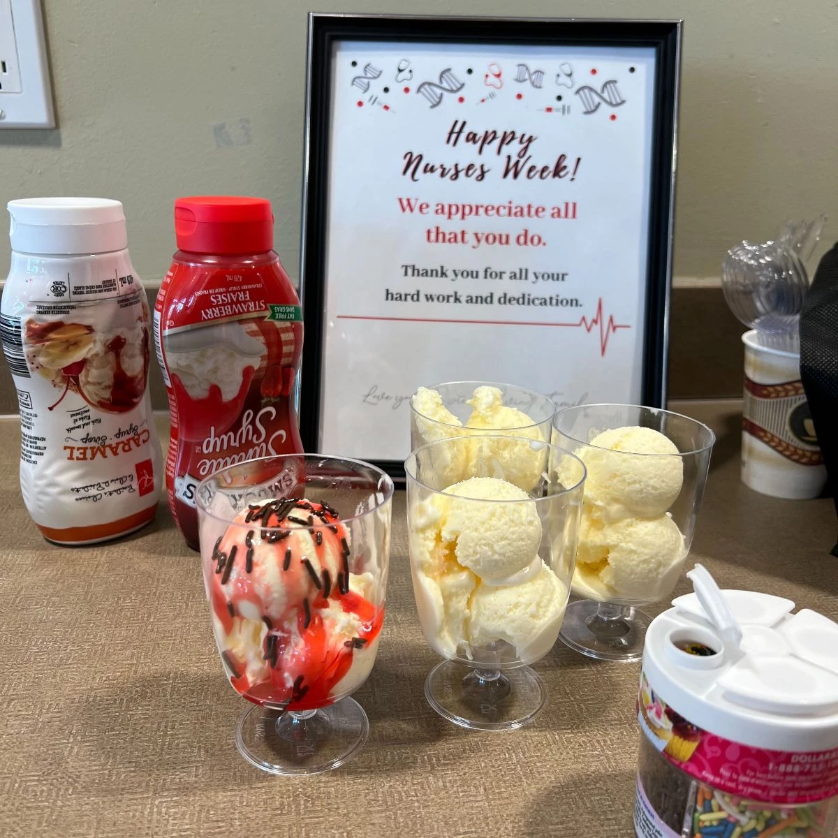 Ice cream sundaes in glasses with strawberry and caramel sauces along with a container of sprinkles.
