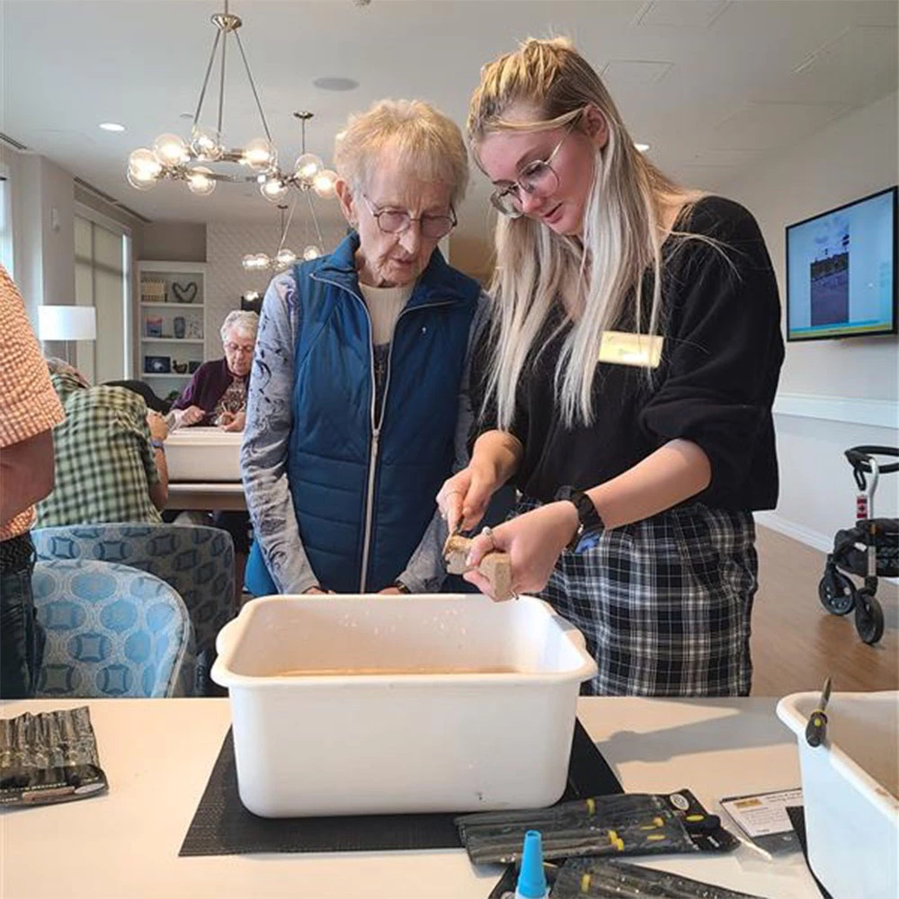 A staff member helps a senior lady clean paintbrushes