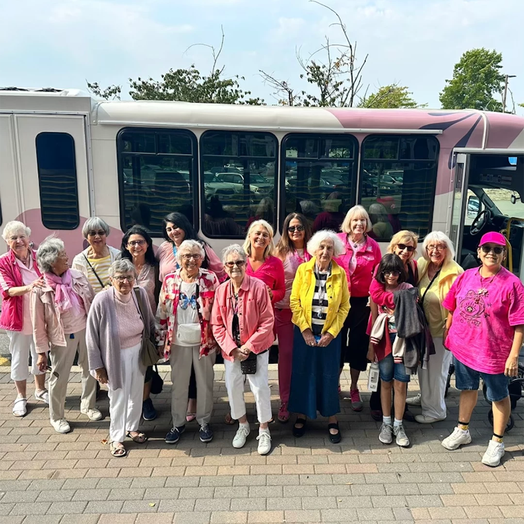 Senior women standing in front of the bus in all pink. They are off to watch the barbie movie!