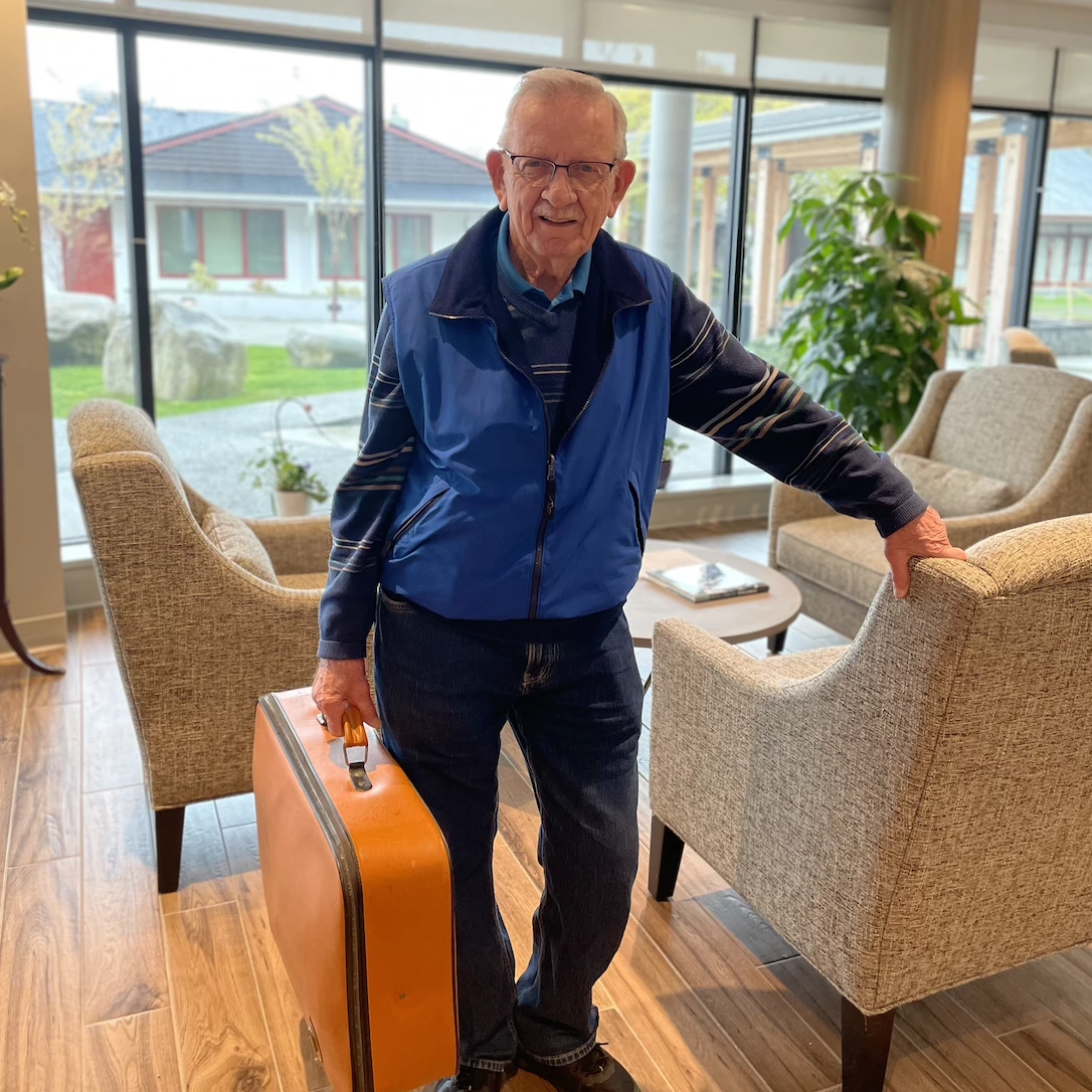 Senior man with an orange suitcase standing in the Wisteria Place library.