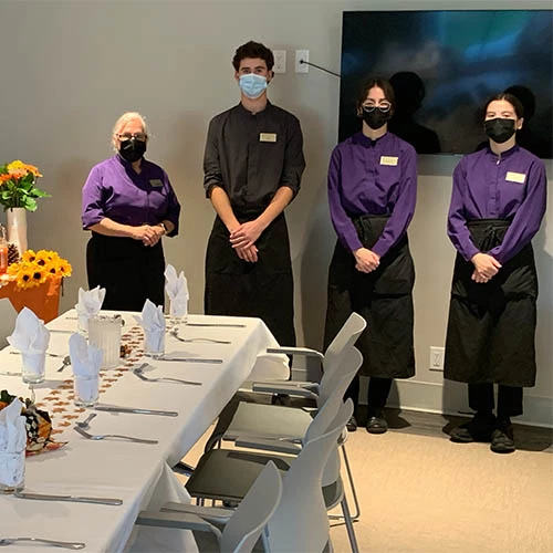 Servers of Wisteria Place standing ready to serve, all are wearing masks.