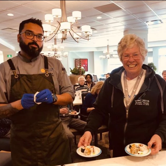 Aster Gardens chef standing with a senior holding two plates of dessert.